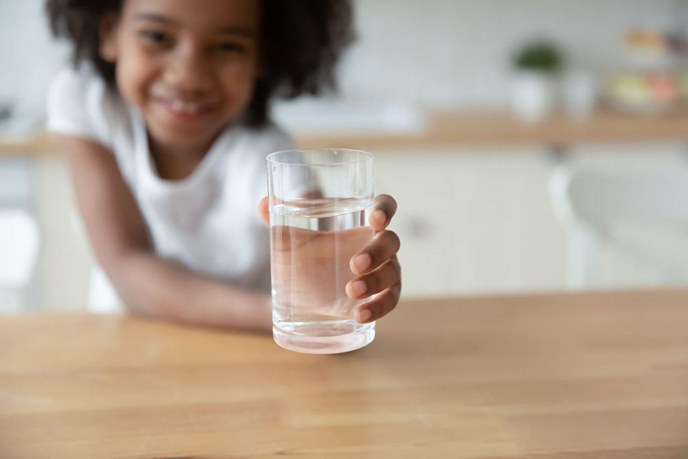 A friendly child holding out her hand for a glass of clean water.