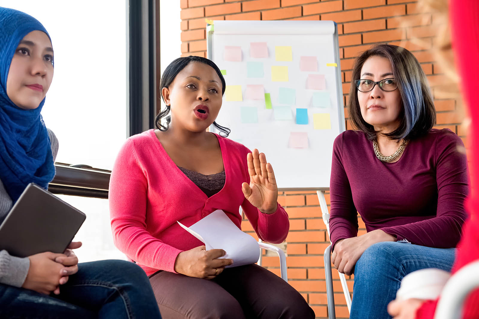 Multiethnic women in colorful casual clothes discuss community policies in a group meeting